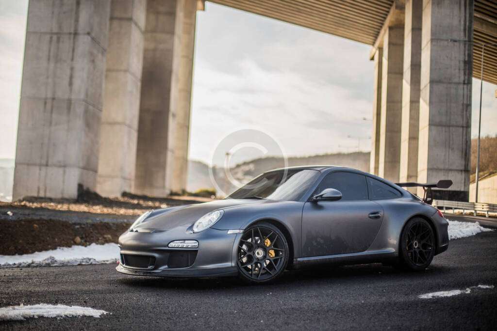 A sleek silver sports car parked under a concrete bridge.