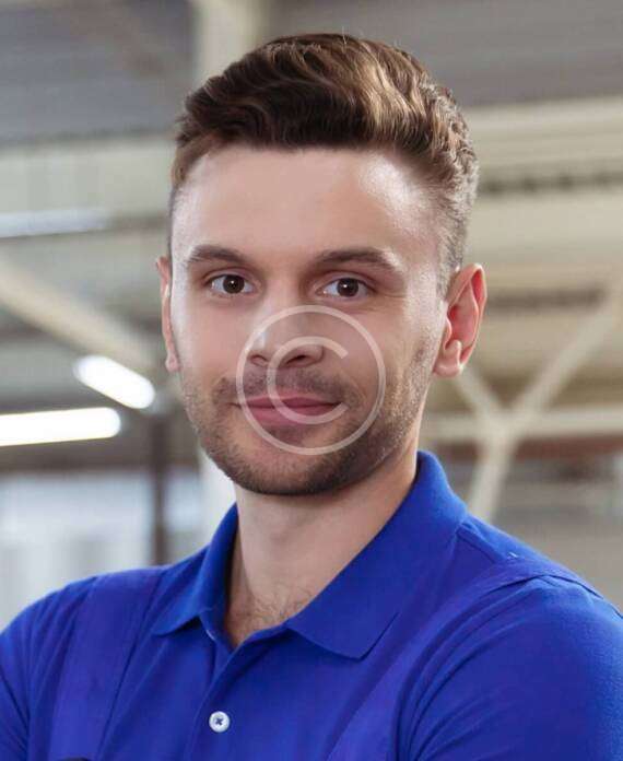 Smiling man in a blue polo shirt standing indoors.