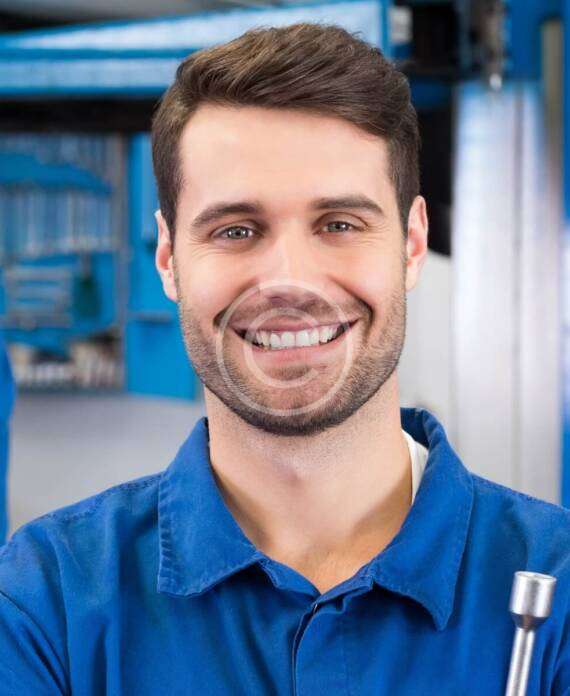Smiling mechanic in blue uniform holding a wrench in a workshop.
