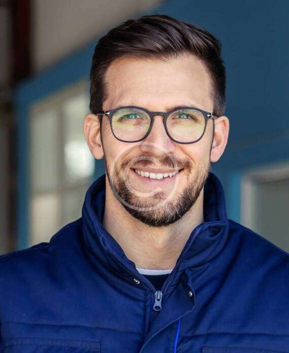 Smiling man wearing glasses and a blue jacket.