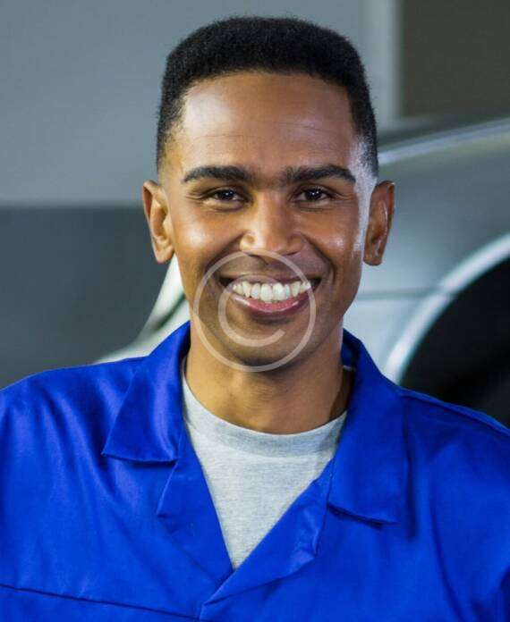 Smiling mechanic in blue uniform near a vehicle.