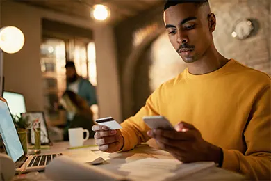 A man shopping online using a credit card and phone.