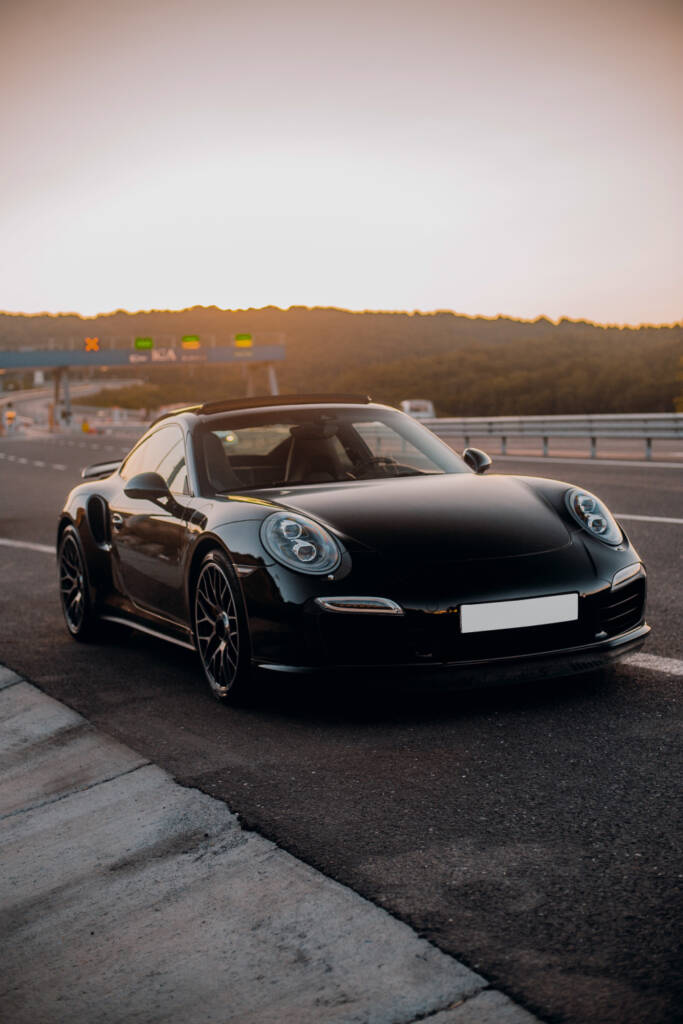 Sleek black sports car parked on a road at sunset.