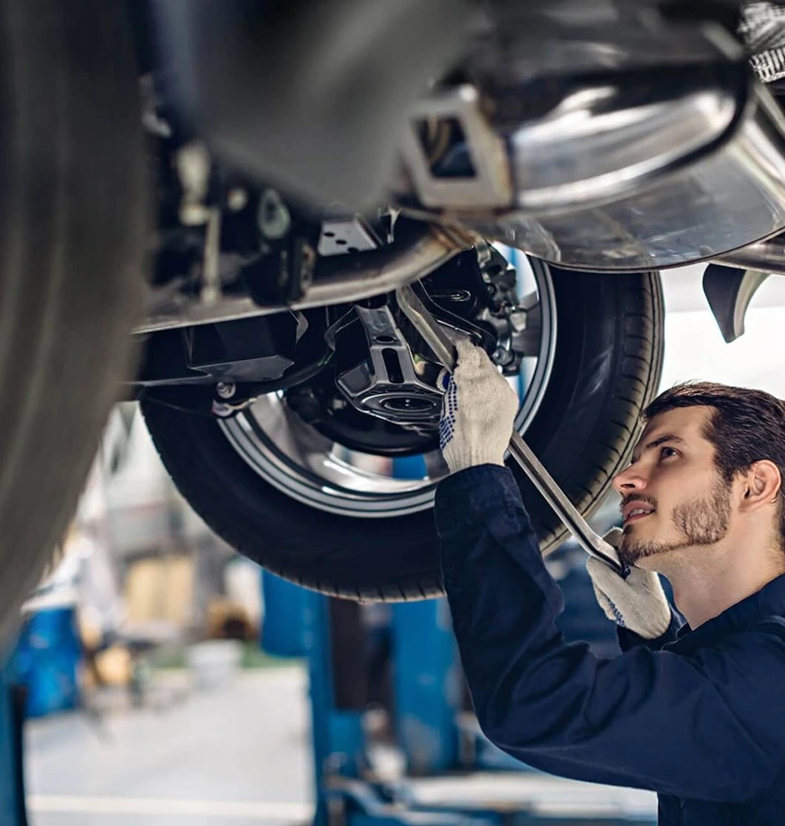 Mechanic inspecting car undercarriage with wrench.