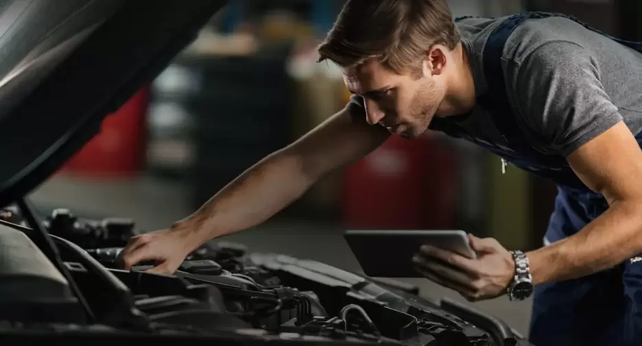 A man inspecting a car engine with a tablet in hand.